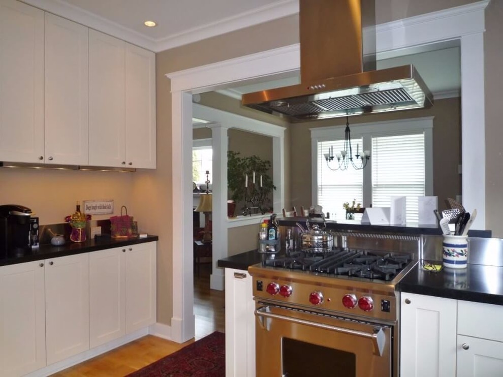 Small transitional u-shaped medium tone wood floor and brown floor enclosed kitchen photo in Seattle with a double-bowl sink, recessed-panel cabinets, white cabinets, stainless steel appliances and black countertops