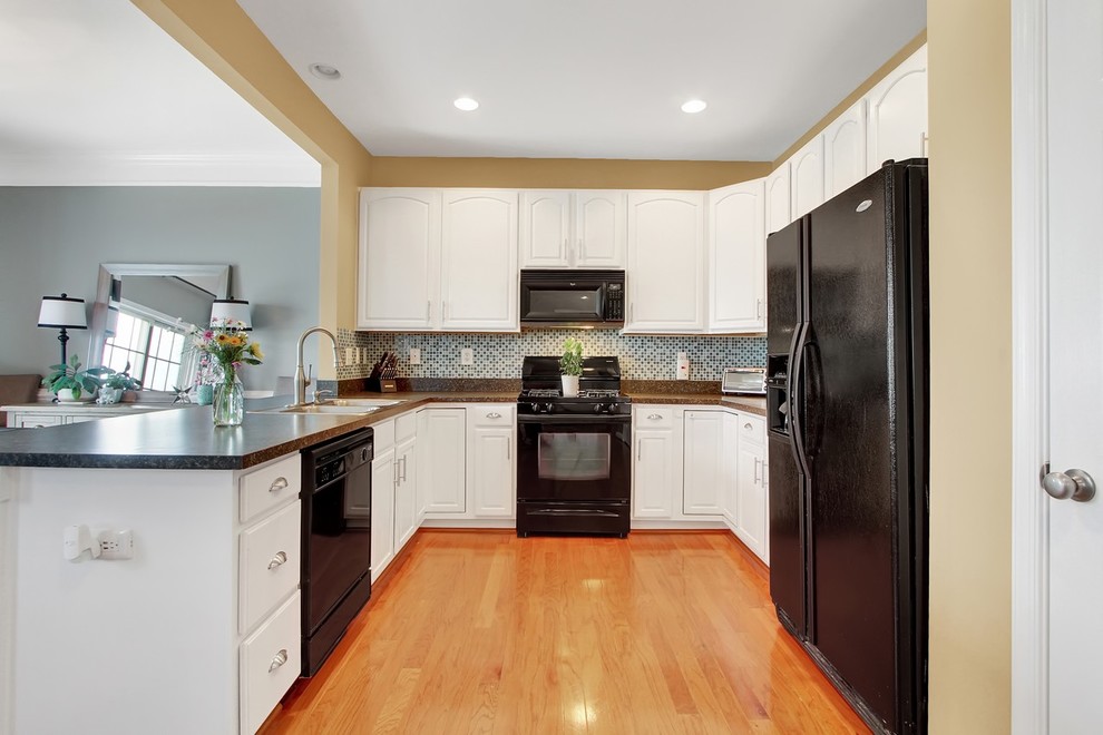 Design ideas for a mid-sized transitional u-shaped eat-in kitchen in Baltimore with a double-bowl sink, recessed-panel cabinets, white cabinets, granite benchtops, multi-coloured splashback, glass tile splashback, black appliances, light hardwood floors, a peninsula and orange floor.