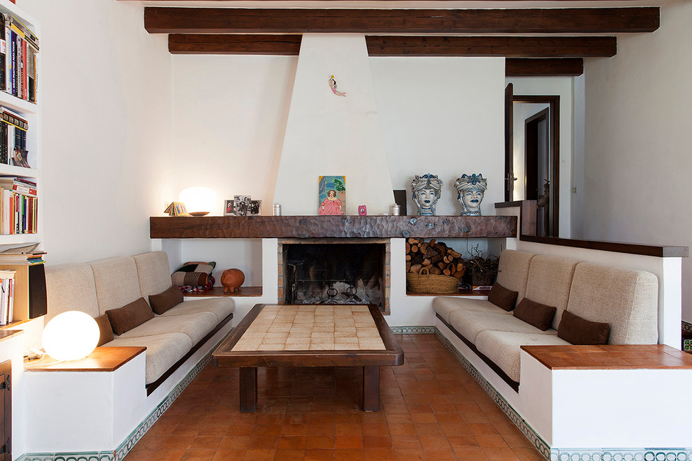 Photo of a mediterranean enclosed living room in Barcelona with a library, white walls, terra-cotta floors and a standard fireplace.