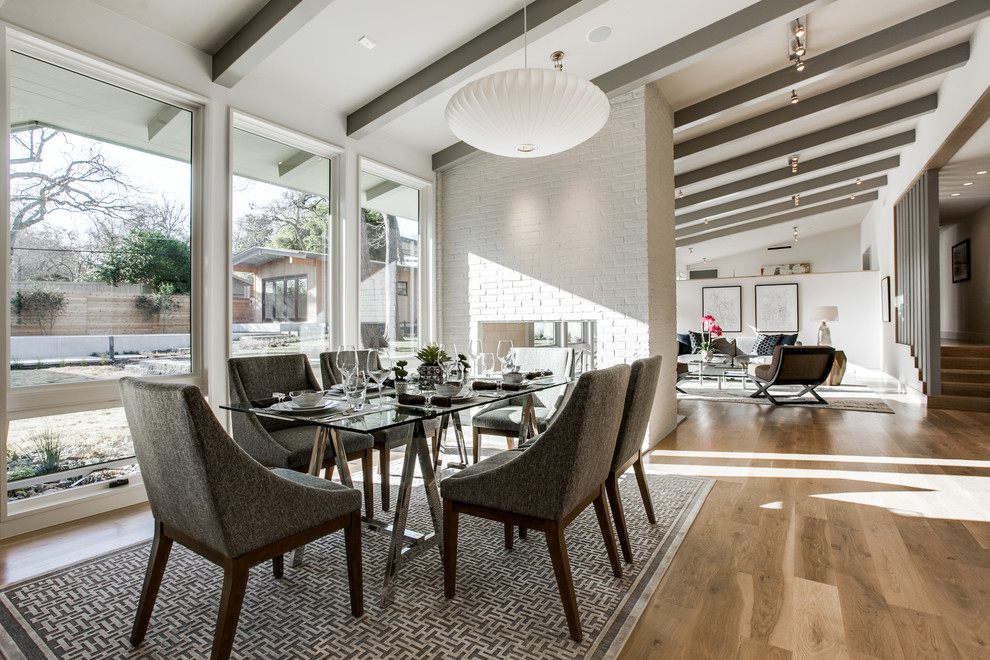 Mid-sized midcentury separate dining room in Dallas with white walls, medium hardwood floors, a two-sided fireplace, a brick fireplace surround and brown floor.