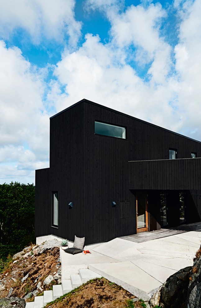 This is an example of a large scandinavian two-storey black exterior in Stockholm with wood siding and a shed roof.
