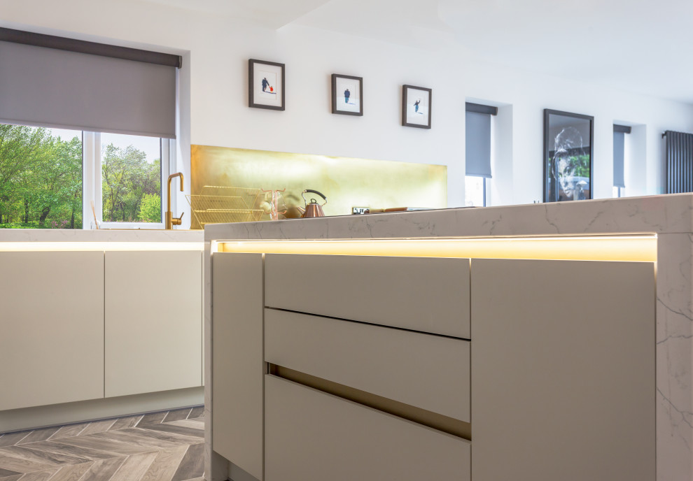 Large contemporary open plan kitchen in Manchester with an integrated sink, flat-panel cabinets, beige cabinets, marble benchtops, metallic splashback, metal splashback, stainless steel appliances, porcelain floors, with island, multi-coloured floor and white benchtop.