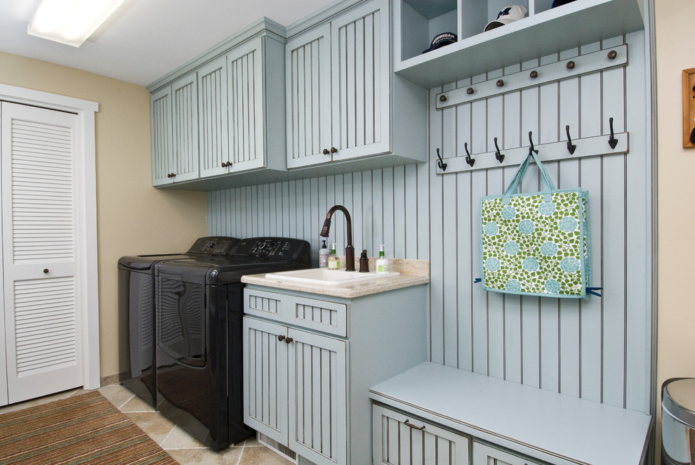 This is an example of a mid-sized traditional single-wall utility room in Other with blue cabinets, a drop-in sink, granite benchtops, beige walls, porcelain floors, a side-by-side washer and dryer, beige floor, beige benchtop and recessed-panel cabinets.