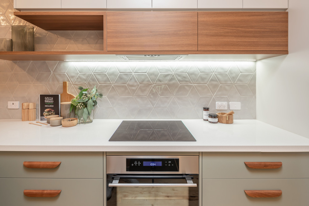 This is an example of a mid-sized contemporary galley kitchen pantry in Adelaide with an undermount sink, flat-panel cabinets, green cabinets, quartz benchtops, grey splashback, porcelain splashback, stainless steel appliances, light hardwood floors, a peninsula and white benchtop.