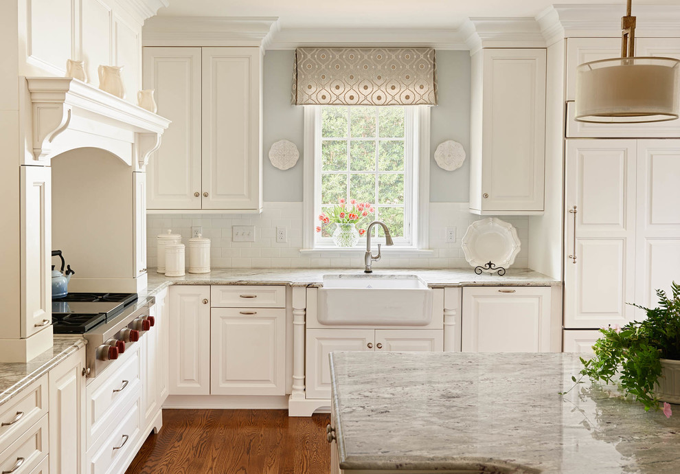 Design ideas for a traditional l-shaped kitchen in Raleigh with a farmhouse sink, raised-panel cabinets, white cabinets, white splashback, subway tile splashback, stainless steel appliances, medium hardwood floors and with island.