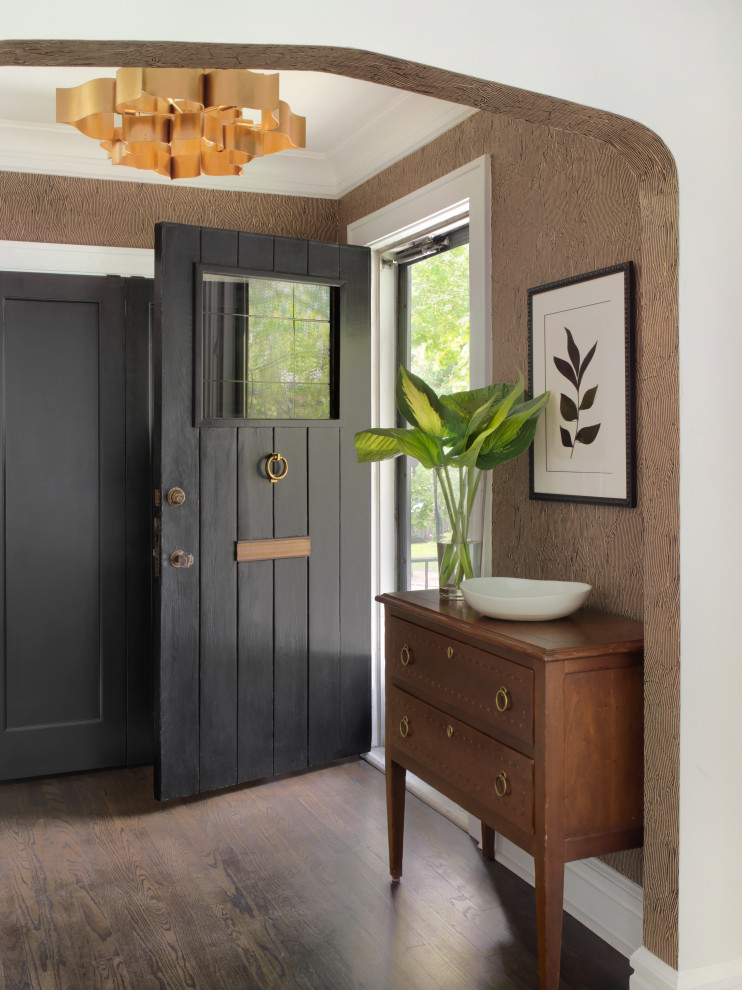 Cette image montre un hall d'entrée vintage de taille moyenne avec un mur marron, parquet foncé, une porte simple, une porte noire et du papier peint.