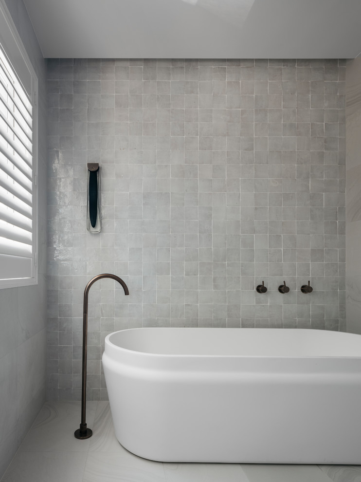 This is an example of a large contemporary master bathroom in Sydney with a freestanding tub, white tile, stone tile, white walls, ceramic floors, an undermount sink, granite benchtops, white floor and white benchtops.