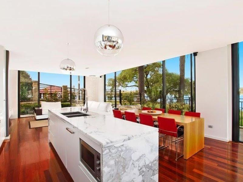 Mid-sized contemporary single-wall open plan kitchen in Sydney with a double-bowl sink, white cabinets, marble benchtops, stainless steel appliances, medium hardwood floors, with island and flat-panel cabinets.
