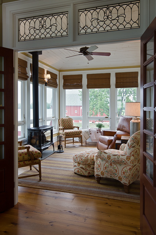 Small country sunroom in Detroit with medium hardwood floors, a wood stove, a standard ceiling and brown floor.