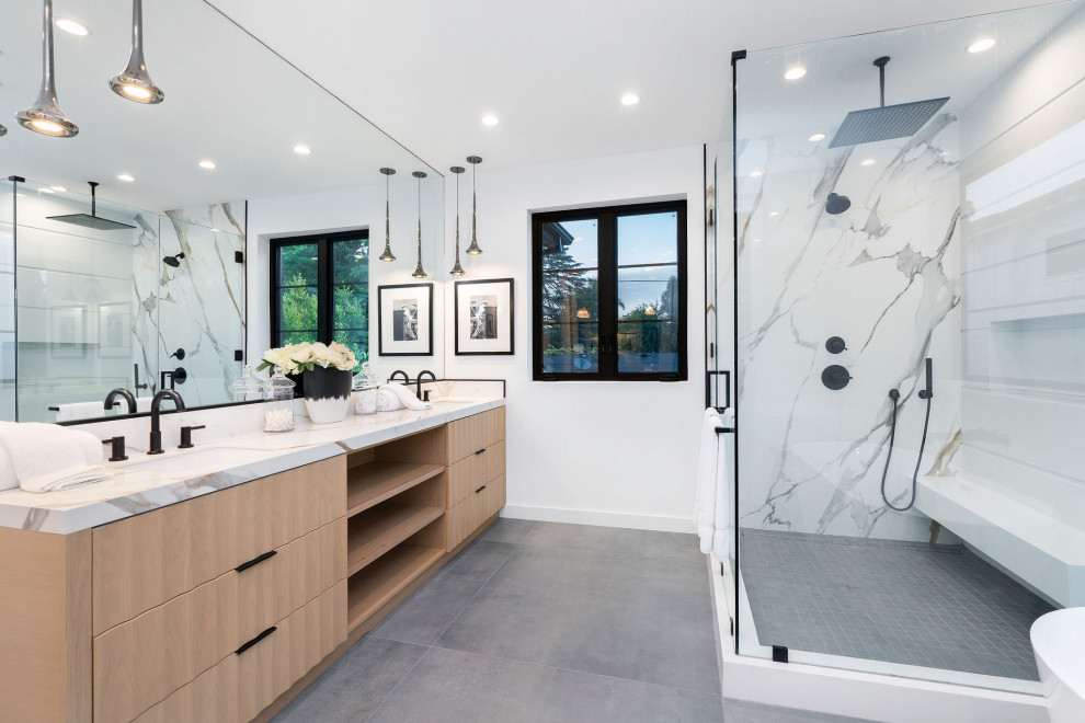Expansive transitional master bathroom in Los Angeles with light wood cabinets, a freestanding tub, a two-piece toilet, white tile, stone slab, porcelain floors, an undermount sink, engineered quartz benchtops, grey floor, a hinged shower door, white benchtops, a shower seat, a double vanity and a built-in vanity.