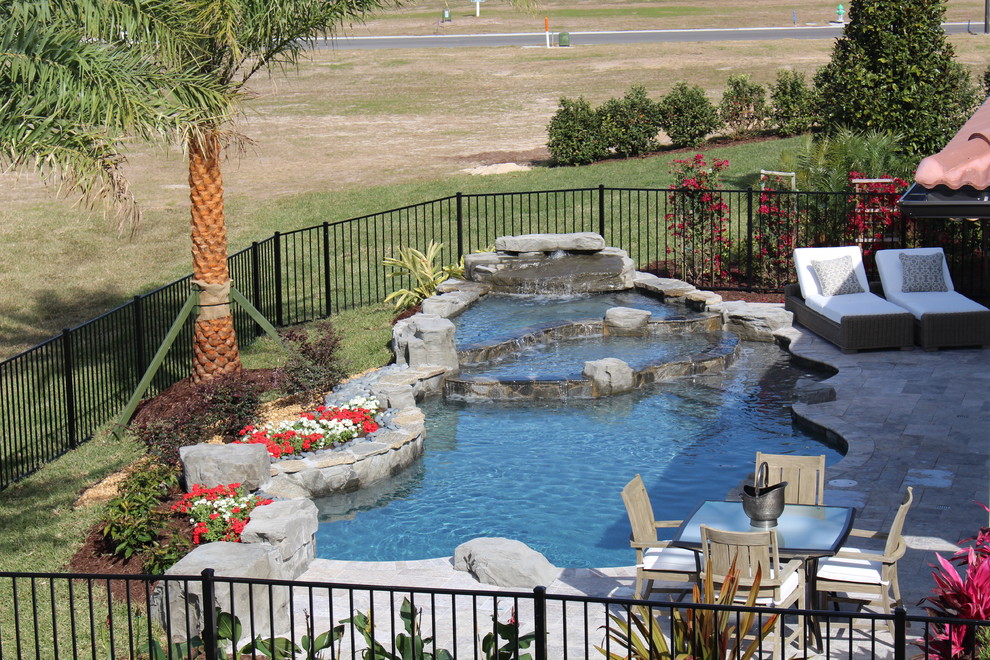 Inspiration for a tropical backyard custom-shaped pool in Orlando with a water feature and natural stone pavers.