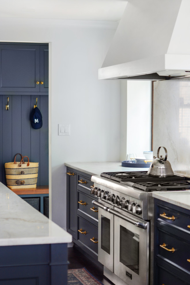 Klassisk inredning av ett stort vit vitt kök och matrum, med en undermonterad diskho, skåp i shakerstil, blå skåp, bänkskiva i kvartsit, vitt stänkskydd, stänkskydd i sten, integrerade vitvaror, mörkt trägolv, en köksö och brunt golv