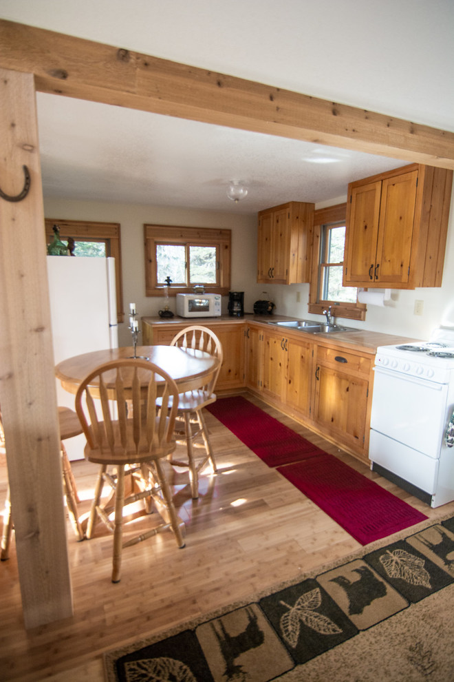 Small country l-shaped eat-in kitchen in Other with a double-bowl sink, shaker cabinets, medium wood cabinets, solid surface benchtops, white appliances, medium hardwood floors, no island and brown floor.