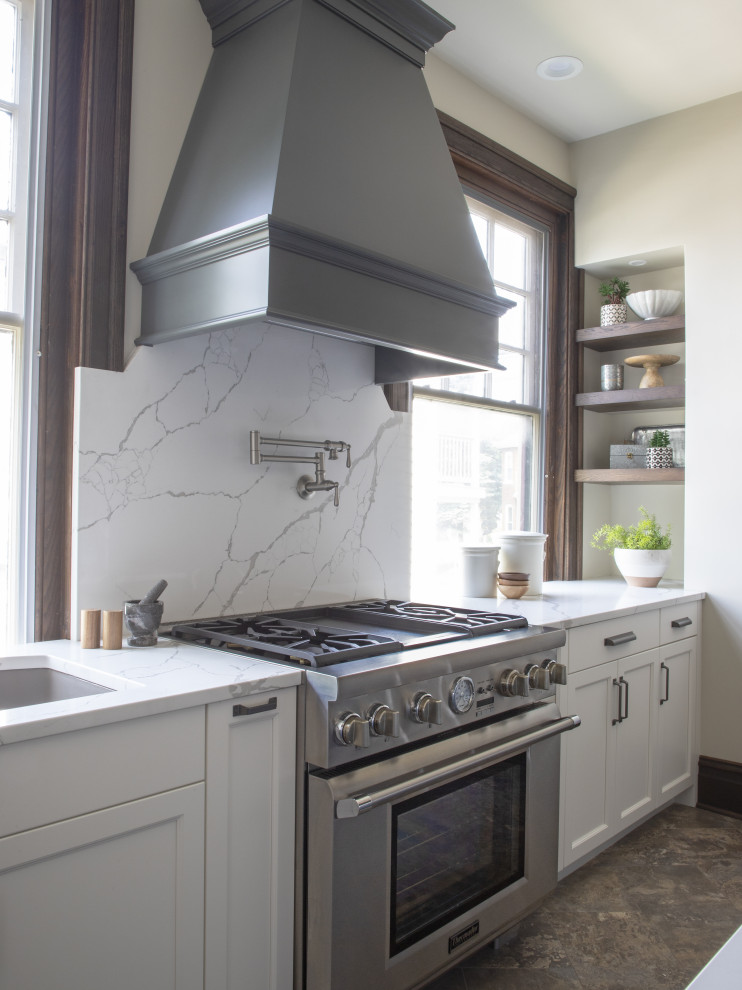 Example of a transitional l-shaped kitchen design with an undermount sink, white backsplash, stone slab backsplash, stainless steel appliances, an island and white countertops