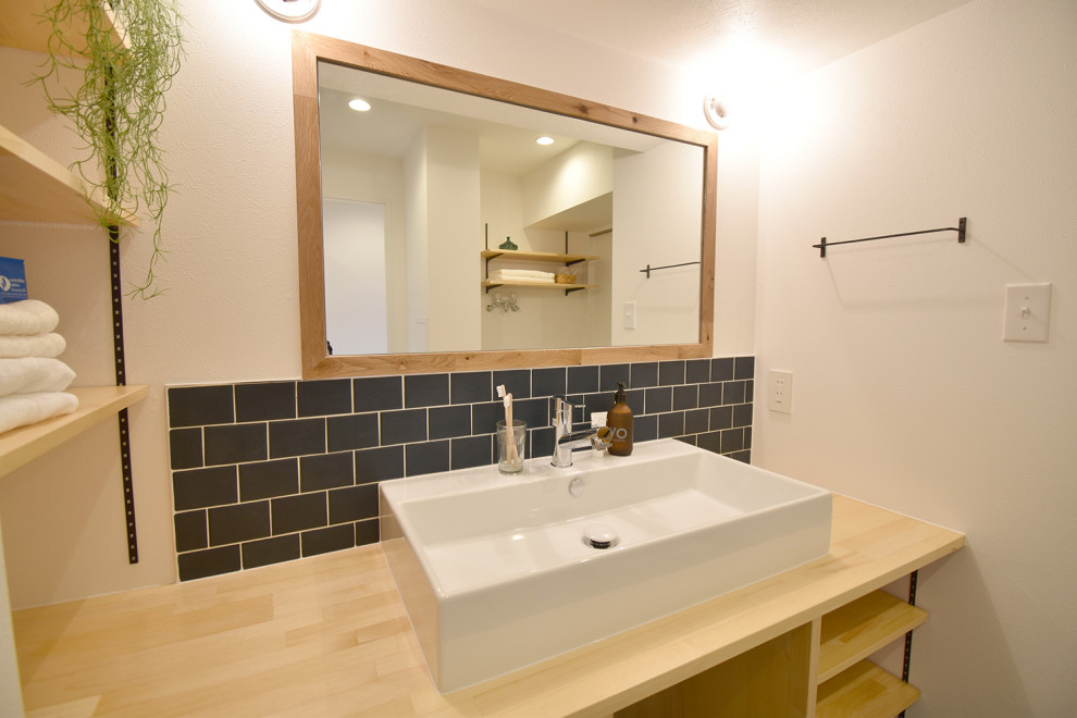 Idee per un bagno di servizio di medie dimensioni con ante in legno chiaro, piastrelle nere e top beige