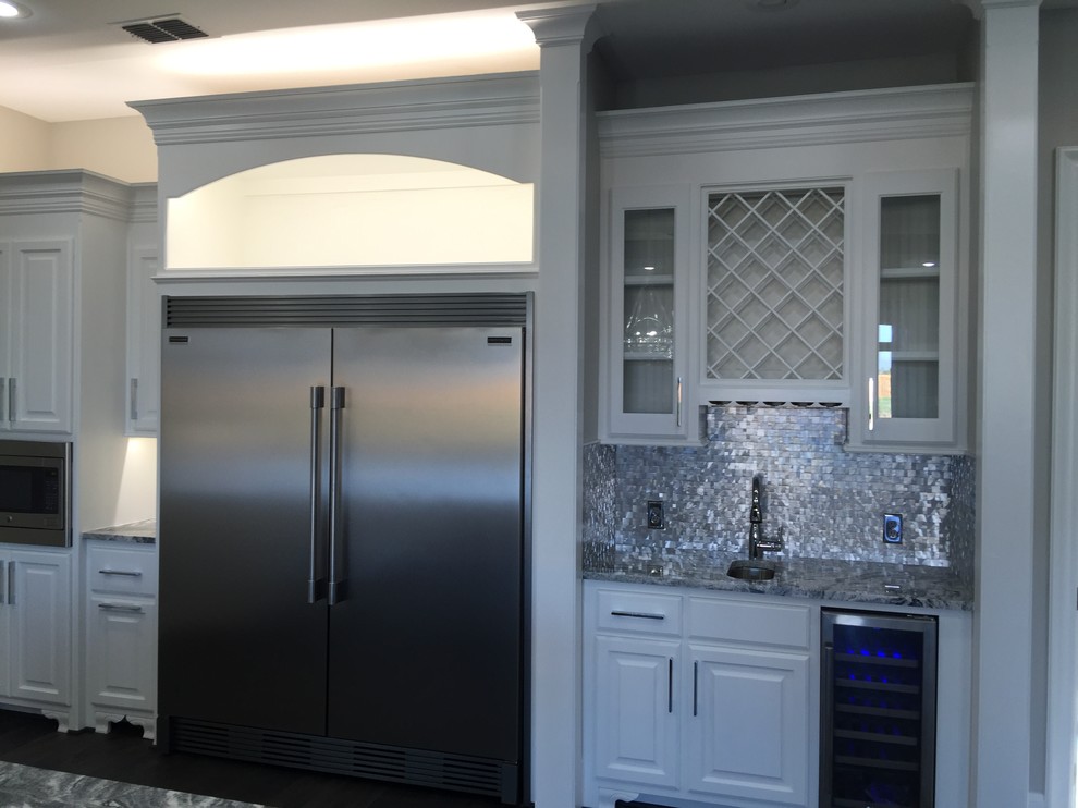 Inspiration for a mid-sized transitional l-shaped dark wood floor open concept kitchen remodel in Orange County with a farmhouse sink, raised-panel cabinets, white cabinets, marble countertops, metallic backsplash, metal backsplash, stainless steel appliances and an island