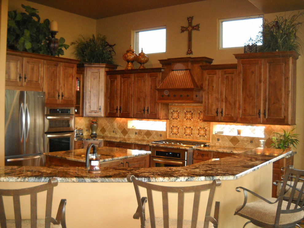 Eat-in kitchen - large mediterranean travertine floor eat-in kitchen idea with an undermount sink, raised-panel cabinets, medium tone wood cabinets, granite countertops, beige backsplash, stone tile backsplash, stainless steel appliances, beige walls and an island
