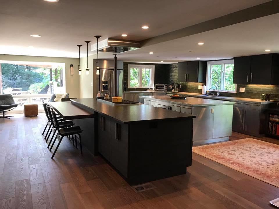 Photo of a large modern l-shaped eat-in kitchen in New York with an undermount sink, flat-panel cabinets, black cabinets, green splashback, subway tile splashback, stainless steel appliances, dark hardwood floors, multiple islands, brown floor and zinc benchtops.