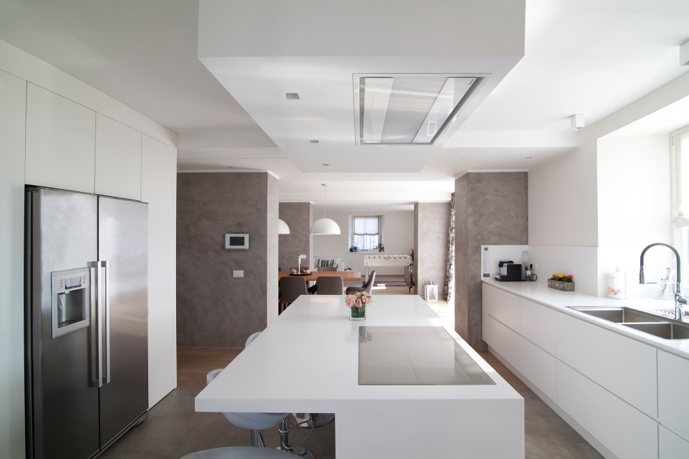 Mid-sized modern single-wall open plan kitchen in Other with an integrated sink, flat-panel cabinets, white cabinets, solid surface benchtops, stainless steel appliances, with island and white benchtop.