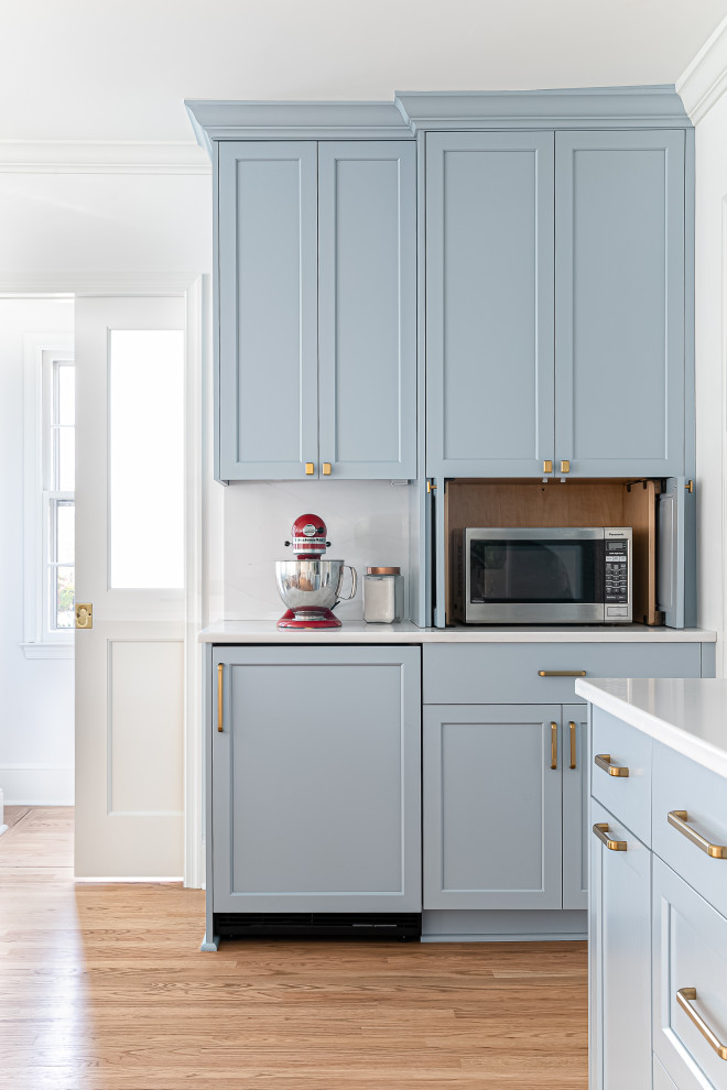 シャーロットにある高級な広いトランジショナルスタイルのおしゃれなキッチン (エプロンフロントシンク、シェーカースタイル扉のキャビネット、青いキャビネット、クオーツストーンカウンター、白いキッチンパネル、クオーツストーンのキッチンパネル、シルバーの調理設備、淡色無垢フローリング、白いキッチンカウンター) の写真