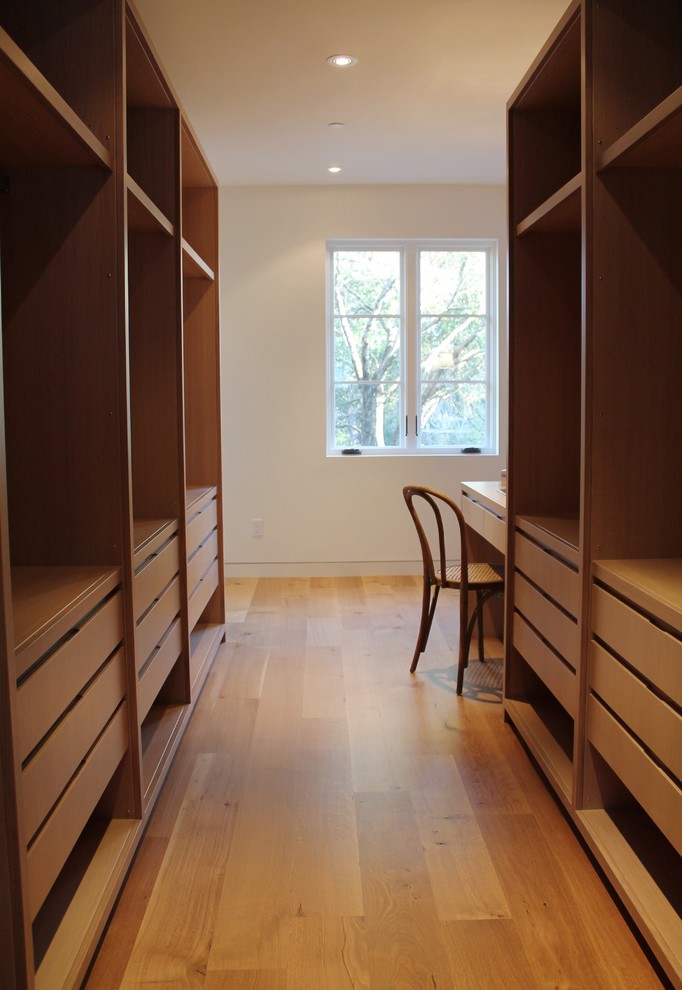This is an example of a mid-sized mediterranean gender-neutral walk-in wardrobe in San Francisco with flat-panel cabinets, light wood cabinets and light hardwood floors.