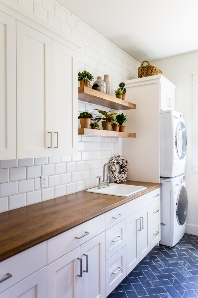 Photo of a large country single-wall dedicated laundry room in Salt Lake City with a single-bowl sink, wood benchtops, white splashback, subway tile splashback, white walls, a stacked washer and dryer, blue floor and brown benchtop.