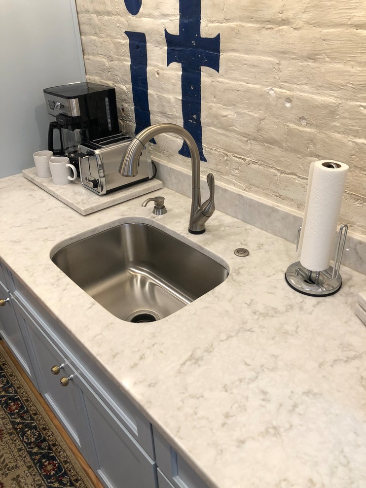 Example of a small transitional single-wall light wood floor and brown floor open concept kitchen design with an undermount sink, recessed-panel cabinets, gray cabinets, marble countertops, white backsplash, brick backsplash, stainless steel appliances, no island and gray countertops