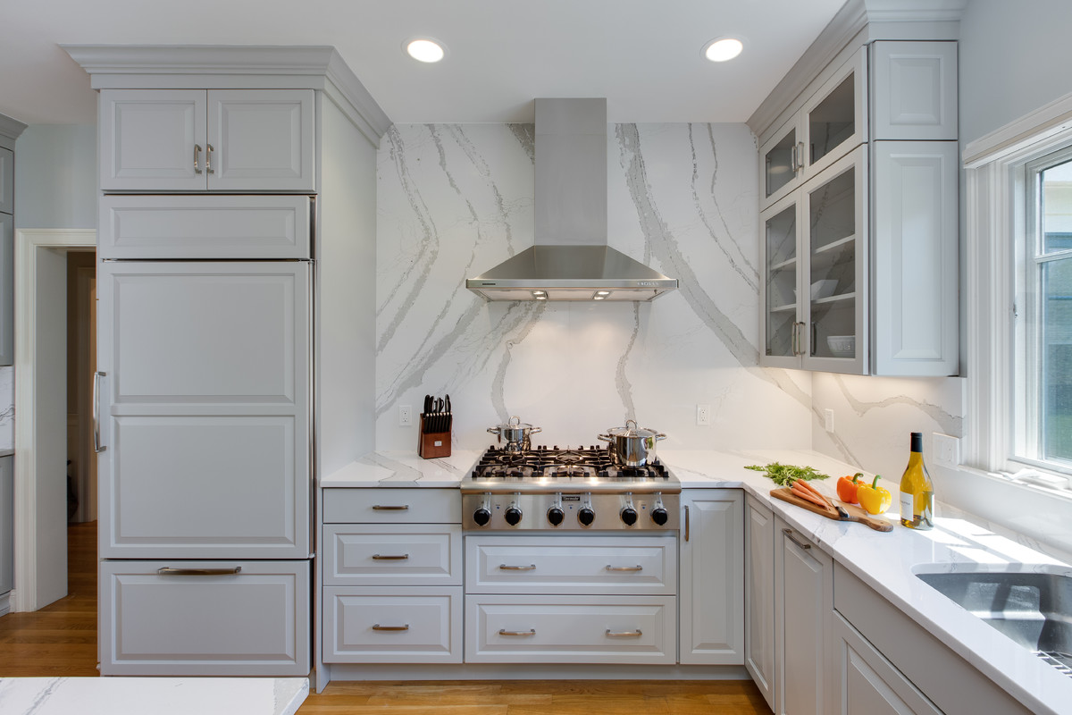 Example of a large transitional l-shaped medium tone wood floor open concept kitchen design in Boston with an undermount sink, raised-panel cabinets, gray cabinets, quartz countertops, stone slab backsplash, paneled appliances and an island