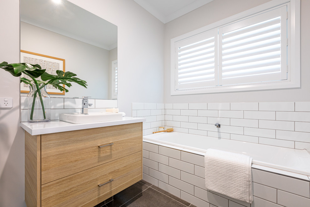 Contemporary 3/4 bathroom in Other with flat-panel cabinets, medium wood cabinets, a drop-in tub, subway tile, a vessel sink, grey floor and white benchtops.
