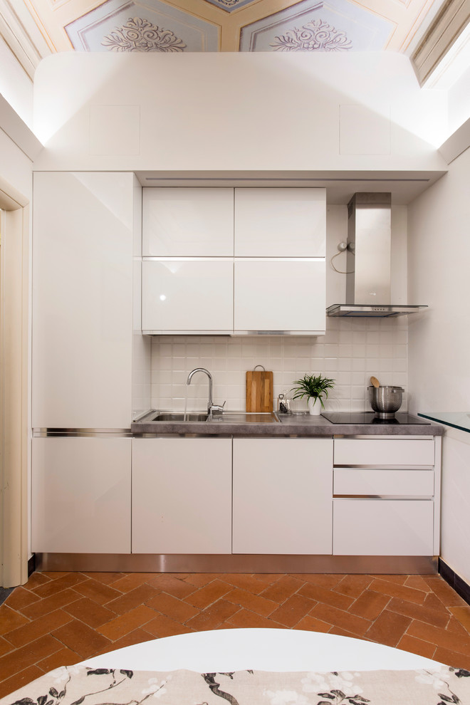 This is an example of a small contemporary single-wall kitchen in Florence with flat-panel cabinets, white cabinets, white splashback, no island, grey benchtop, a single-bowl sink and orange floor.