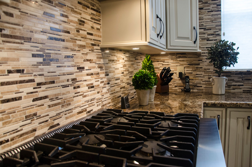 Example of a large transitional l-shaped porcelain tile open concept kitchen design in Miami with a farmhouse sink, raised-panel cabinets, white cabinets, granite countertops, multicolored backsplash, mosaic tile backsplash, stainless steel appliances and an island