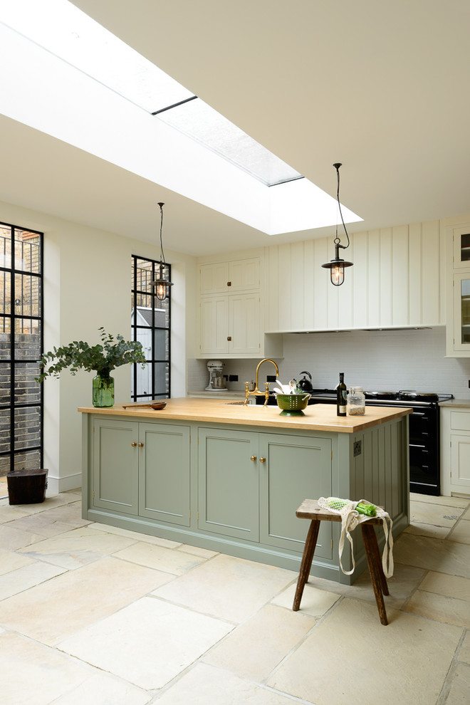 Inspiration for a large transitional open plan kitchen in London with a farmhouse sink, beaded inset cabinets, white cabinets, wood benchtops, white splashback, subway tile splashback, black appliances and with island.