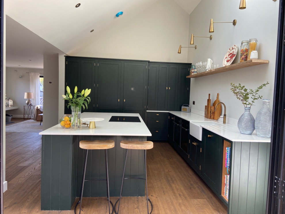 Modern inredning av ett stort vit vitt kök och matrum, med en rustik diskho, luckor med profilerade fronter, bänkskiva i kvarts, svarta vitvaror, en köksö och brunt golv