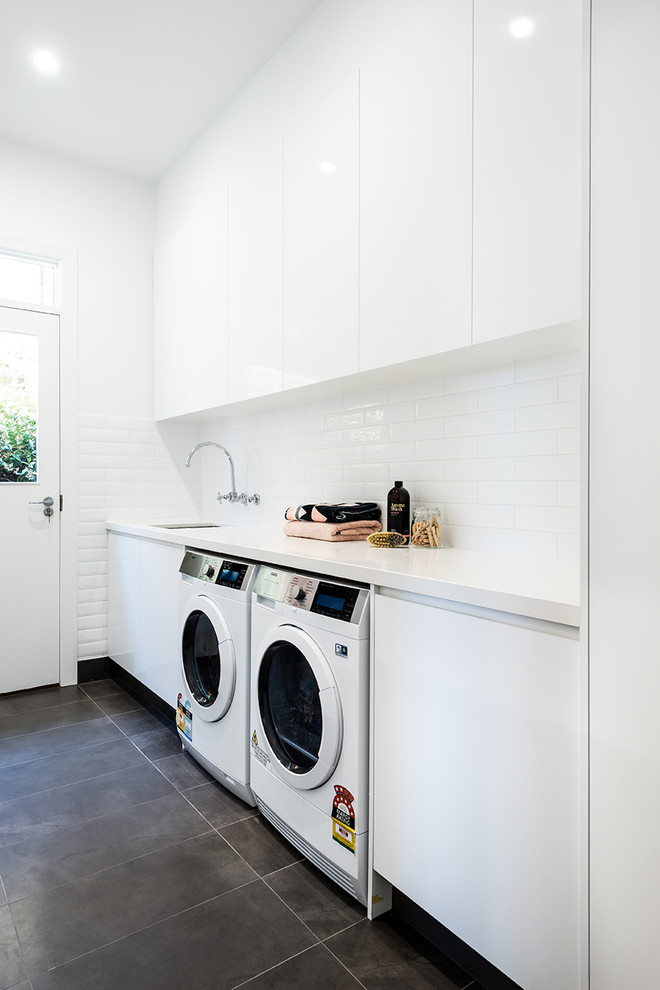 Photo of a mid-sized contemporary single-wall utility room in Melbourne with an undermount sink, flat-panel cabinets, white cabinets, quartz benchtops, white walls, ceramic floors, a side-by-side washer and dryer and grey floor.
