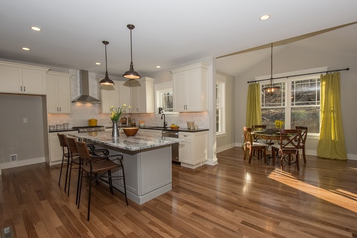 Mid-sized transitional l-shaped eat-in kitchen in Philadelphia with an undermount sink, shaker cabinets, white cabinets, granite benchtops, beige splashback, stone tile splashback, stainless steel appliances, medium hardwood floors, with island and brown floor.