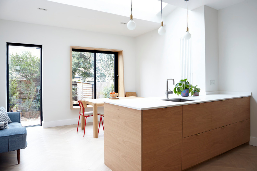 Design ideas for a mid-sized contemporary single-wall eat-in kitchen in London with an undermount sink, flat-panel cabinets, light wood cabinets, quartzite benchtops, multi-coloured splashback, cement tile splashback, panelled appliances, light hardwood floors, with island and white benchtop.