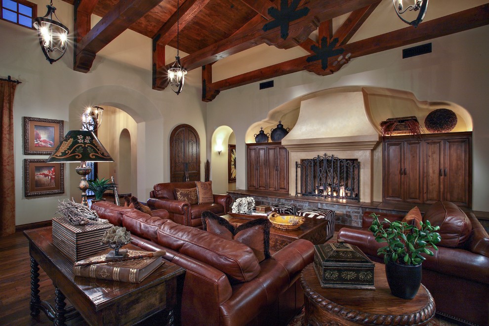 Design ideas for an expansive mediterranean open concept living room in Phoenix with beige walls, dark hardwood floors, a standard fireplace, a plaster fireplace surround, a concealed tv and brown floor.