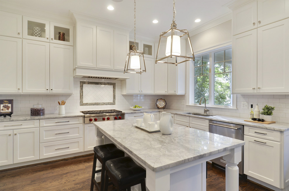 Example of a transitional dark wood floor and brown floor kitchen design with white backsplash, subway tile backsplash and stainless steel appliances