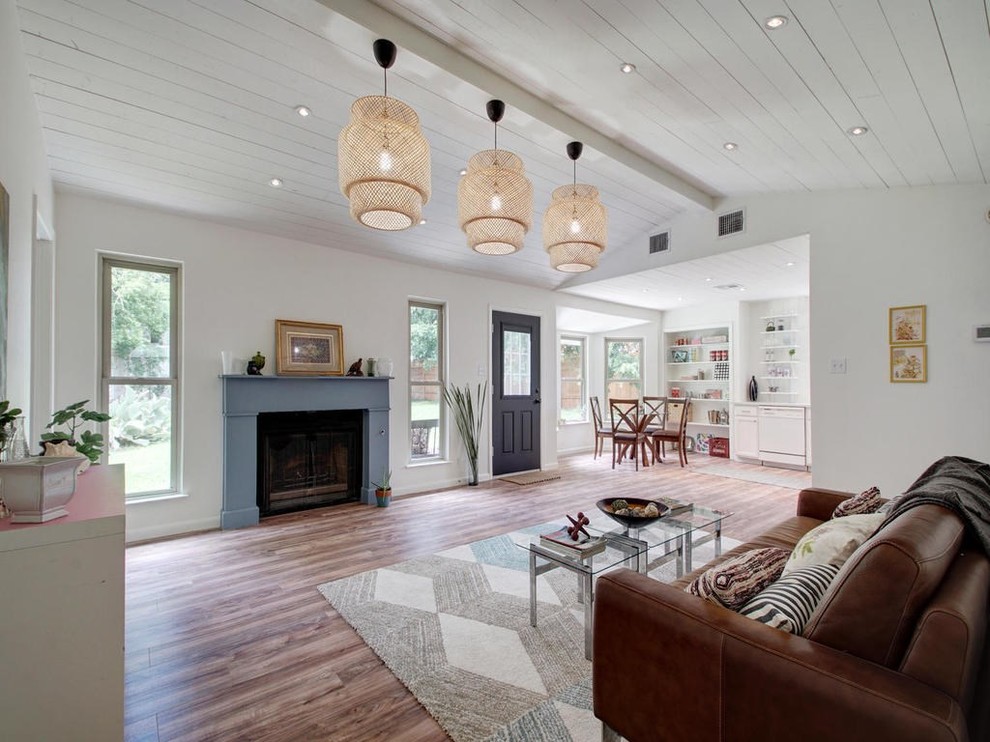 Design ideas for a mid-sized country open concept living room in Austin with white walls, laminate floors, a wood stove, a wood fireplace surround and brown floor.