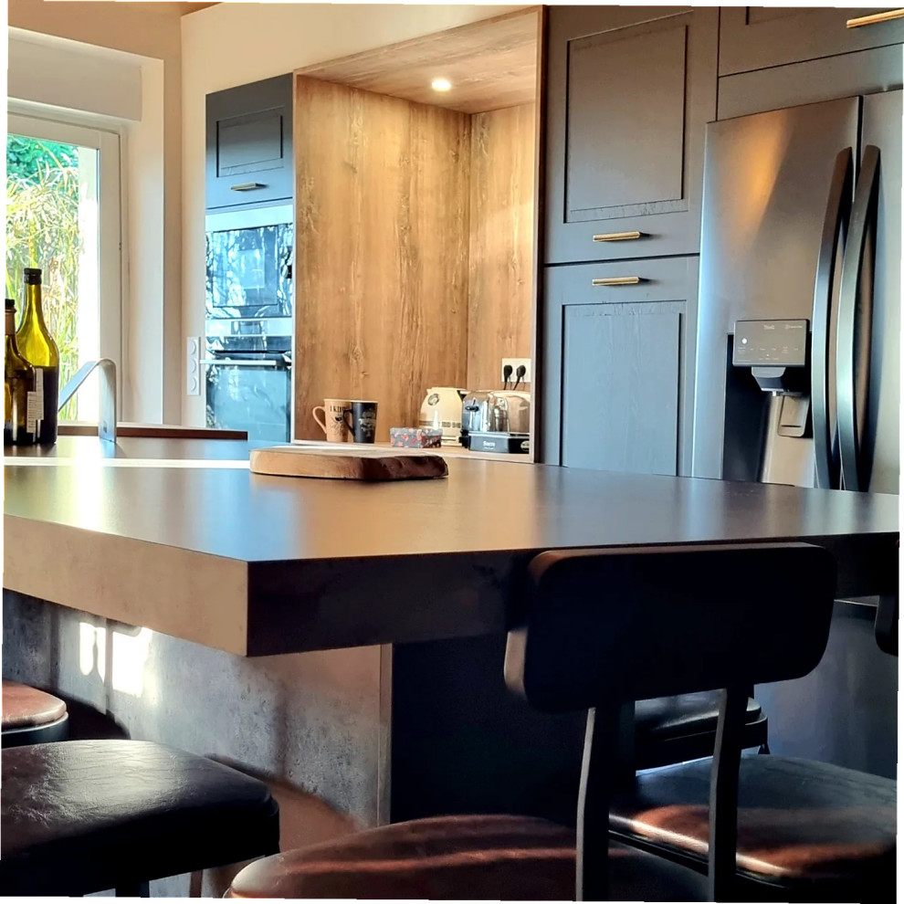 ボルドーにある高級な広いカントリー風のおしゃれなキッチン (ドロップインシンク、フラットパネル扉のキャビネット、青いキャビネット、ラミネートカウンター、茶色いキッチンパネル、木材のキッチンパネル、シルバーの調理設備、セラミックタイルの床、マルチカラーの床、黒いキッチンカウンター、表し梁) の写真