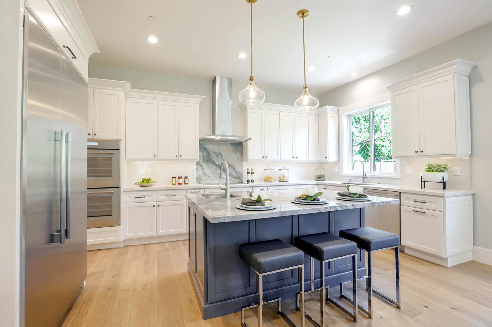 Foto på ett stort maritimt blå kök, med en undermonterad diskho, skåp i shakerstil, vita skåp, bänkskiva i kvartsit, vitt stänkskydd, stänkskydd i keramik, ljust trägolv, en köksö och brunt golv