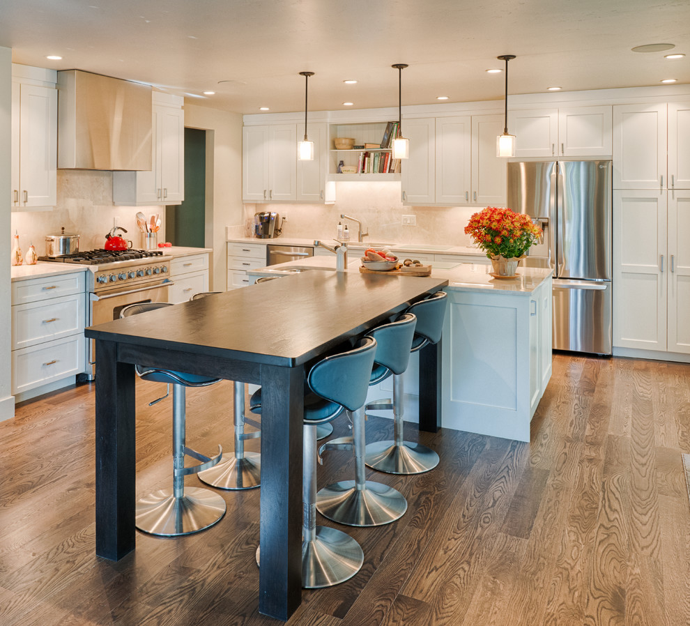 Photo of a mid-sized contemporary l-shaped open plan kitchen in Denver with a drop-in sink, shaker cabinets, white cabinets, granite benchtops, white splashback, stainless steel appliances, plywood floors and multiple islands.