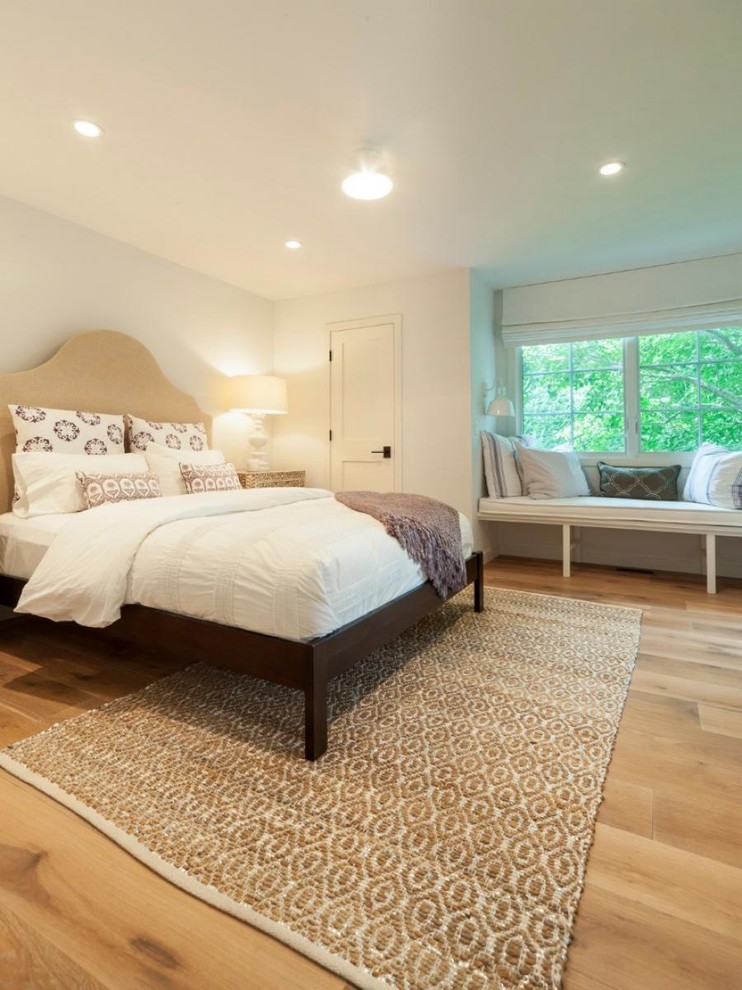 Large contemporary master bedroom in New York with white walls and medium hardwood floors.