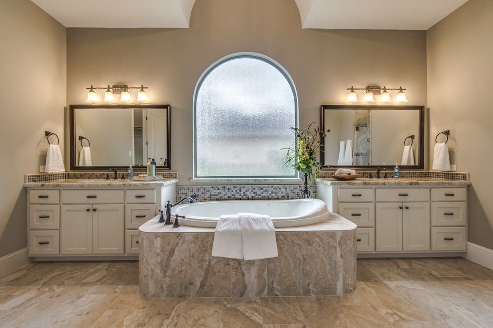 Inspiration for a large mediterranean master bathroom in Houston with an undermount sink, granite benchtops, furniture-like cabinets, white cabinets, a hot tub, brown tile, mosaic tile, beige walls, ceramic floors and beige floor.