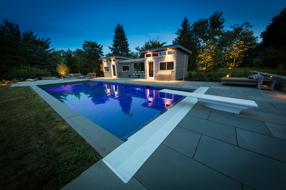 Mid-sized modern backyard rectangular lap pool in Philadelphia with a pool house and natural stone pavers.