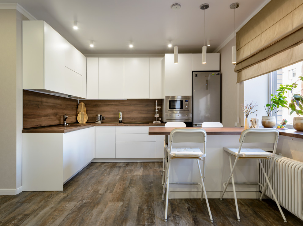 Design ideas for a large contemporary l-shaped kitchen in Novosibirsk with a drop-in sink, flat-panel cabinets, white cabinets, wood benchtops, brown splashback, timber splashback, stainless steel appliances, vinyl floors, brown floor, brown benchtop and a peninsula.