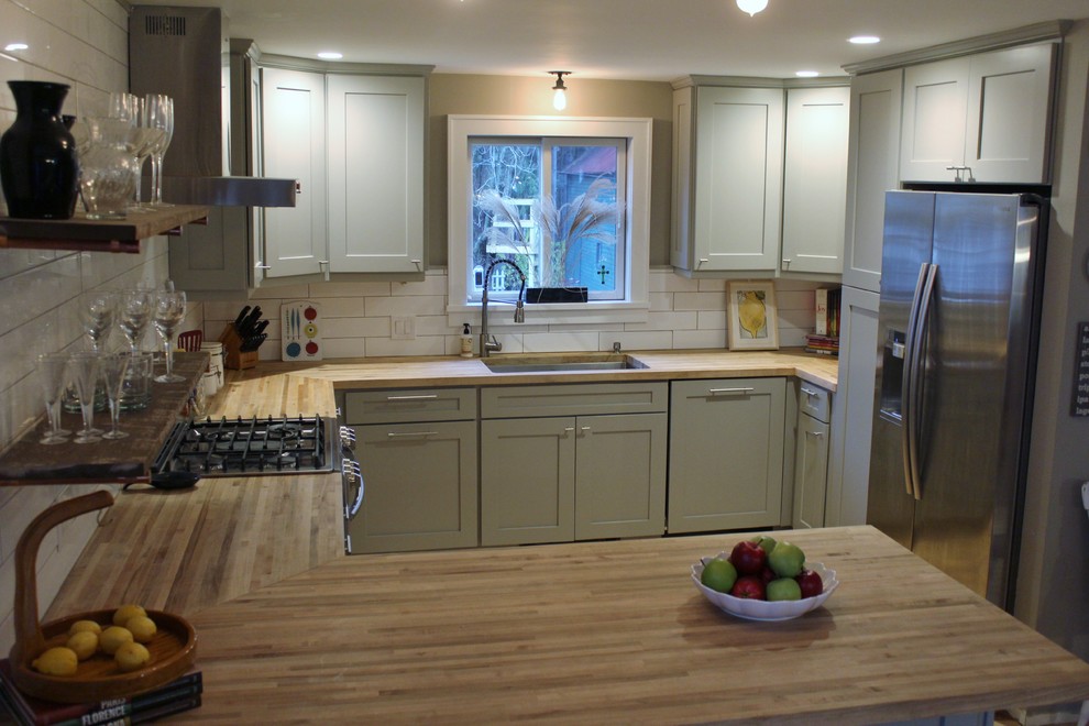 Mid-sized country u-shaped eat-in kitchen in Boston with shaker cabinets, wood benchtops, white splashback, subway tile splashback, stainless steel appliances, a peninsula, brown floor, an undermount sink, green cabinets and light hardwood floors.