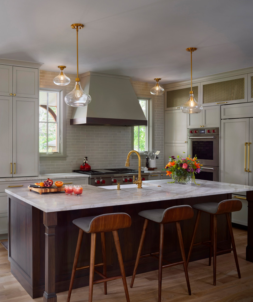 Transitional l-shaped medium tone wood floor and brown floor kitchen photo in Denver with a farmhouse sink, recessed-panel cabinets, gray cabinets, gray backsplash, subway tile backsplash, paneled appliances, an island and gray countertops