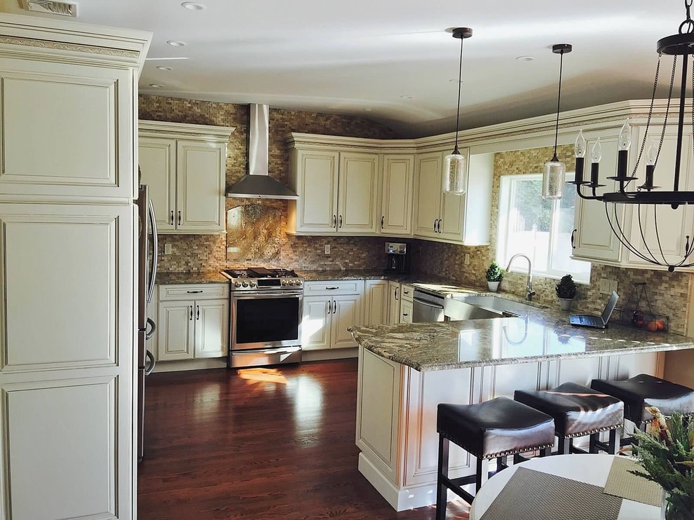 Mid-sized transitional u-shaped dark wood floor open concept kitchen photo in New York with a farmhouse sink, raised-panel cabinets, white cabinets, granite countertops, brown backsplash, stone tile backsplash and stainless steel appliances
