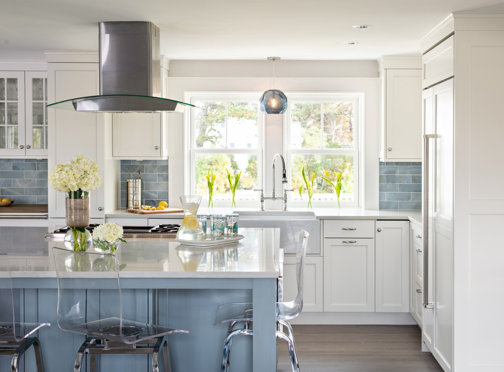 Photo of a beach style l-shaped kitchen in Boston with a farmhouse sink, shaker cabinets, white cabinets, blue splashback, panelled appliances, dark hardwood floors, with island, brown floor and white benchtop.